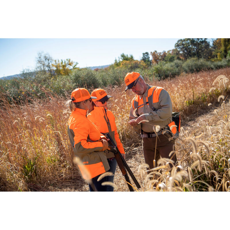 Two women and a man wearing bright orange standing in a field.